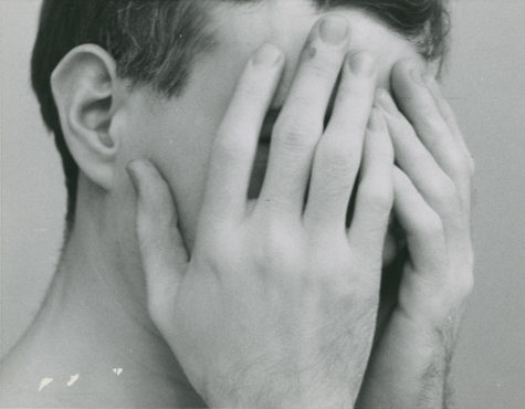 Black-and-white photograph of a young Andy Warhol with his hands covering his face.