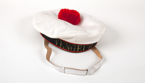 A white hat with a white chin strap and a fluffy, red ball on the top.
