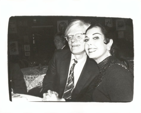 Black-and-white photograph of Andy Warhol and Ann Miller seated side-by-side, looking at the viewer and smiling.