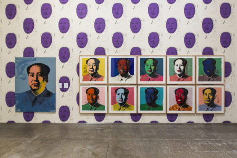 A wall on the fourth floor of The Andy Warhol Museum. The wallpaper is a white background with many reproduction images of Mao Zedong drawn by Andy Warhol. The drawings on the wallpaper are black outline of Mao's profile. His face is painted in purple. The artworks on the wall are eleven various screen prints by Andy Warhol of the same photograph of Mao with various colors of paint used to cover various sections of Mao's face, clothing and the background.