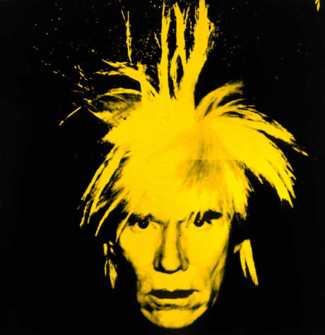 A screen print of Andy Warhol's face looking at the camera on a black background. His face is painted yellow and his hair is sticking up in the middle and out on the sides.