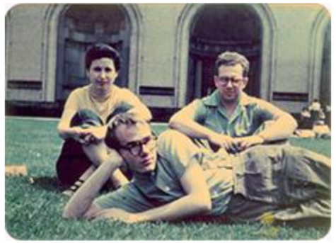 A photograph of Pearlstein, Warhol, and Cantor lounging in campus green spaces at Carnegie Tech. Pearlstein and Cantor sit with their arms around their knees, which they have pulled to their chests. Warhol lays in front of them, propped up on one elbow. In the background, two arches of a campus building are visible.