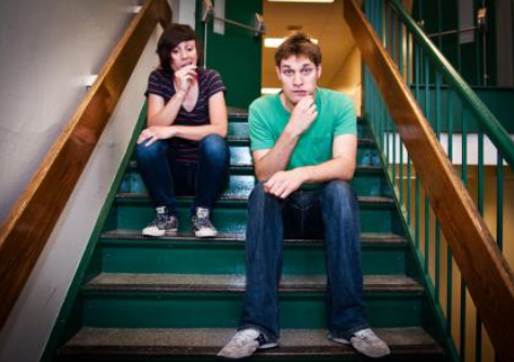A man in a green t-shirt and a woman in a striped v neck t-shirt sit on a green flight of stairs.