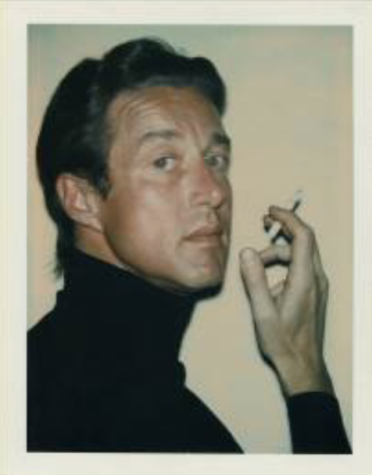A polaroid picture of a young man with short black hair wearing a black turtle neck gazing over his right shoulder toward the camera, the cigarette in his raised hand ready to be put to his lips.