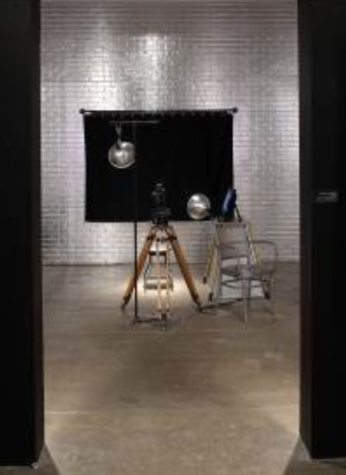 Lights, a black backdrop, and an old film camera are set up in a room lined with silver bricks.