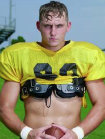 A young man wearing a yellow football jersey stands on a field holding a football in front of him. His jersey is pulled up revealing his stomach and the lower portion of chest padding.