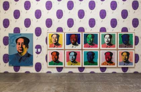 A photograph of a gallery in The Andy Warhol Museum featuring several screen printed portraits of Mao Zedong against a background of wallpaper also created using his likeness.