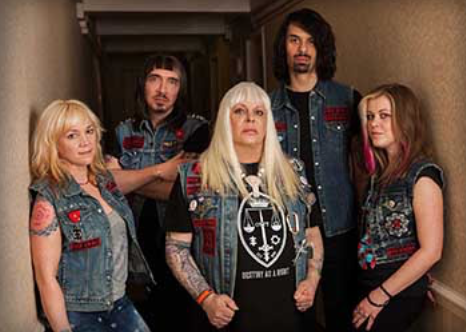 The members of psychic TV gathered in a hallway, all five wearing black t-shirts and denim vests with red embroidery.