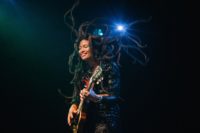 A photo of a woman with long hair on stage smiling and playing guitar.