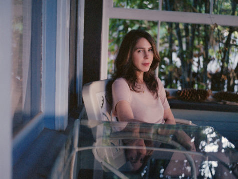A woman with brown hair sitting at a glass patio table. A forest can be seen in the background.