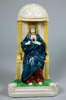 Statue of Jesus sitting on an ornate throne in a blue robe with an exposed heart and bleeding wounds on his hands.