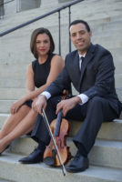 Two people are sitting next to each other on steps. One is holding a violin.