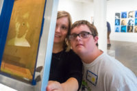 A teen and their parent in The Warhol galleries examine an exposed silkscreen featuring an image of Andy Warhol.