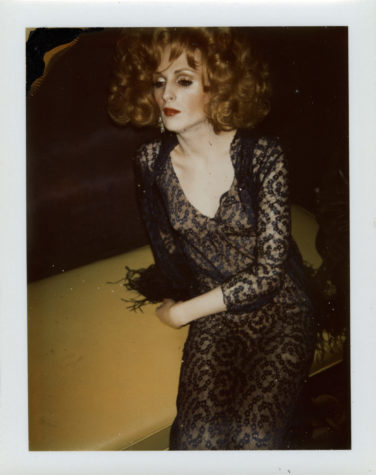 A person in a dress with black accents sits while looking off to the left of the camera.