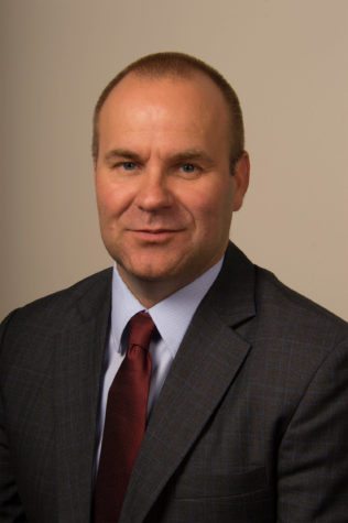 A portrait of a person wearing a suit and smiling towards the camera.