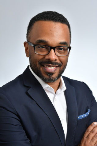 A portrait of a person wearing a suit and smiling towards the camera.