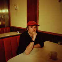 A man wearing a red cap is sitting at a booth staring at the camera.