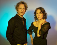Two people standing in front of a colorful background looking at the camera.