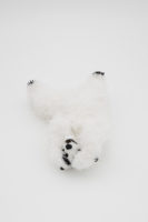 A foam bear sculpture covered in white feathers is upside down holding the sides of its face with its paws.