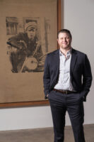 Dan Law stands in a gallery in The Andy Warhol Museum in front of a screenprint artwork by Andy Warhol.