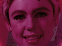 Film still of a close-up of a smiling Edie Sedgwick with a pink tone.