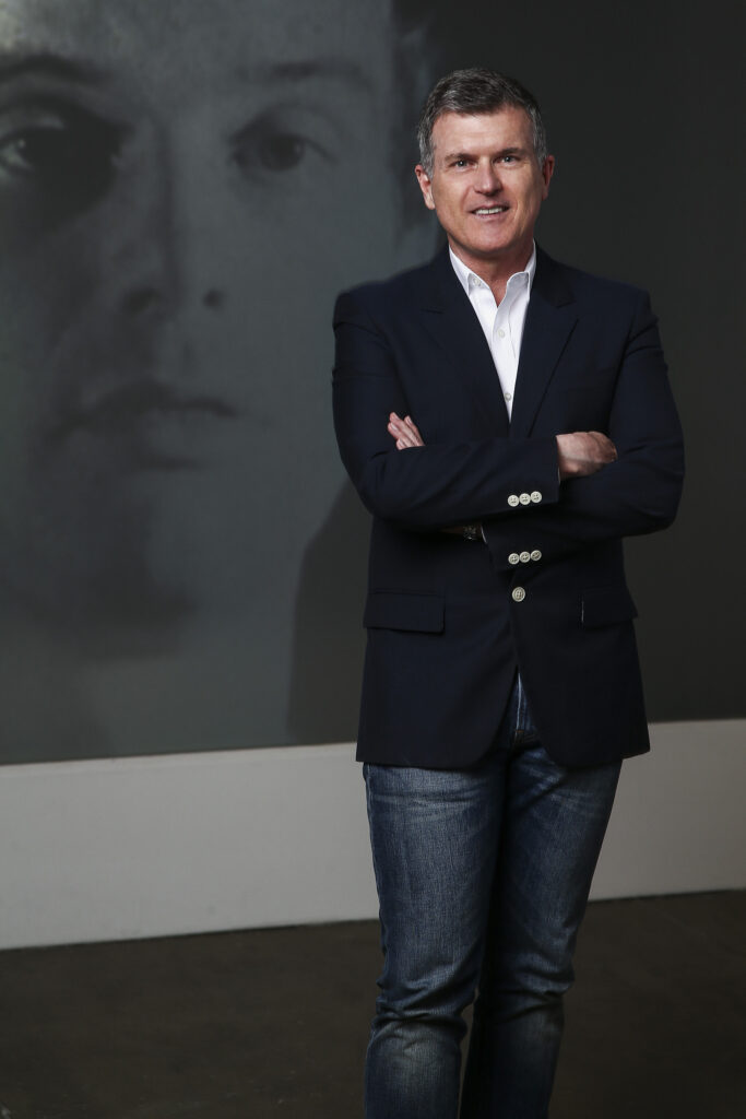 Patrick Moore stands in gallery in The Andy Warhol Museum in front of a black and white film that was currently on a man's face on the wall.