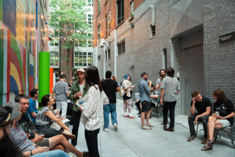Many people gathered outside on Silver Street, the alley behind The Andy Warhol Museum, that includes a mural painted by the artist, Typoe, made up of various colorful shapes on the wall of the museum and part of a wall on the building on the other side of the alley is painted silver.