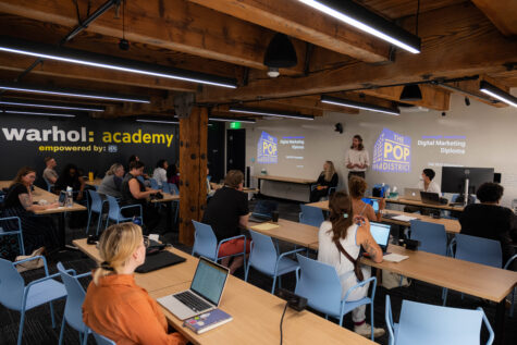 A class of multiple students sitting at desks with laptops as part of The Warhol Academy.