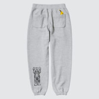 Gray sweatpants with an embroidered cartoon-like figure by the artist KAWS on one leg and a small yellow banana by Andy Warhol coming out of the the upper left pocket.