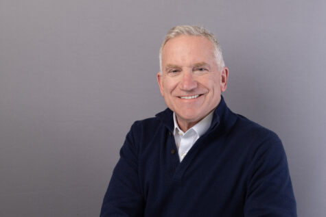 Portrait of a smiling individual in a navy blue shirt, against a neutral gray background.