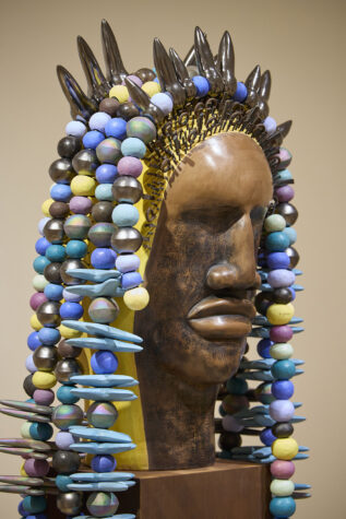 Artistic sculpture featuring a large head adorned with multi-colored beads and metal elements.